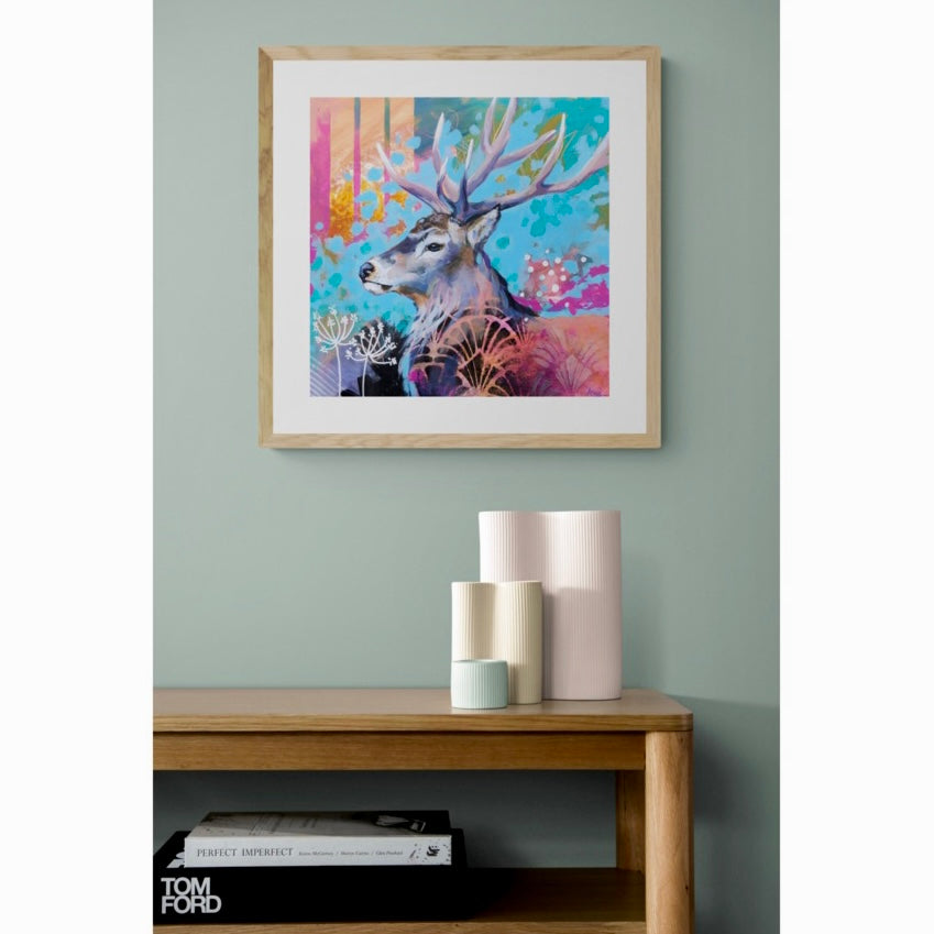 Colourful framed art print of a stag hanging on a duck egg blue wall.
