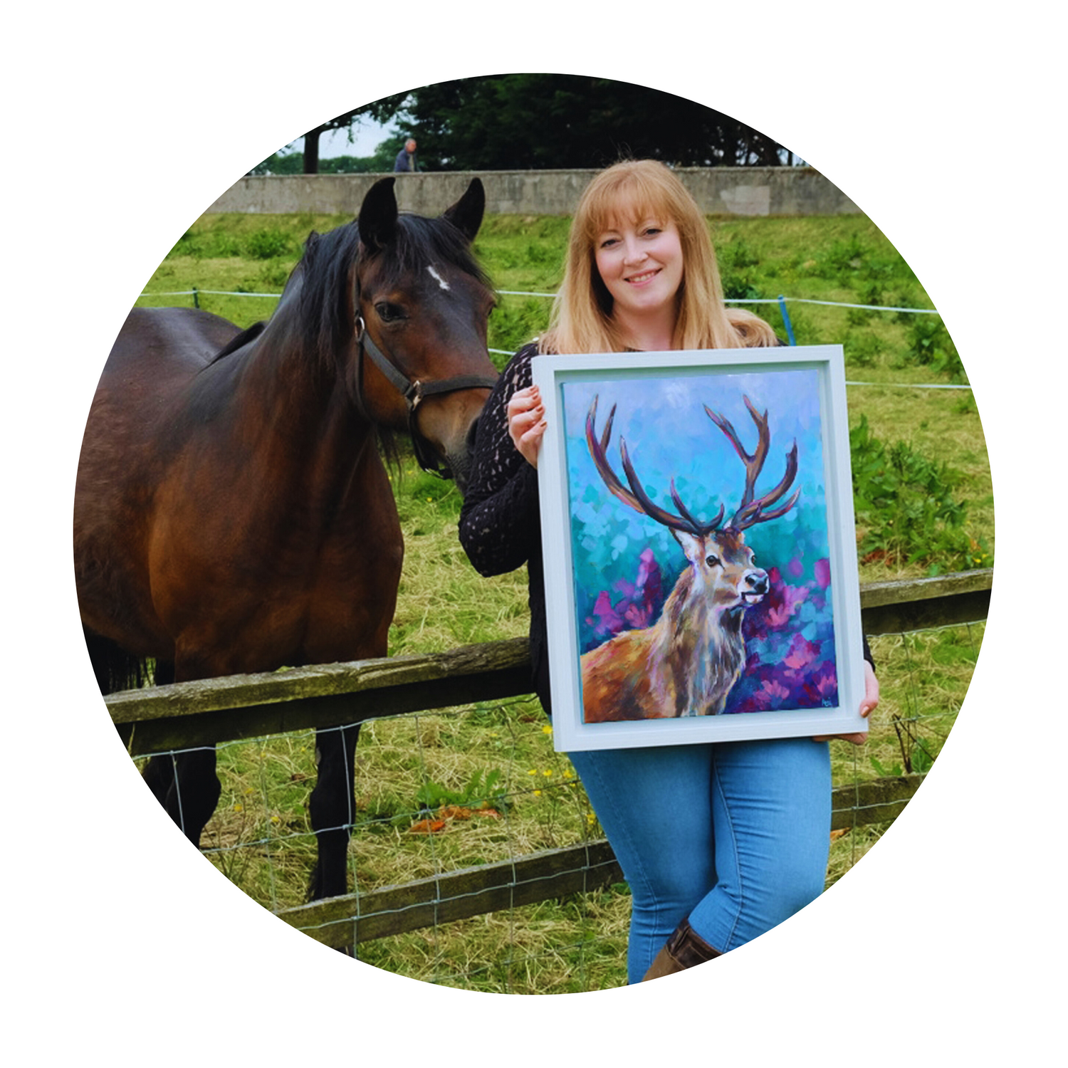 Animal artist Anj Jamieson leans against a fence, displaying her stag painting alongside a bay horse